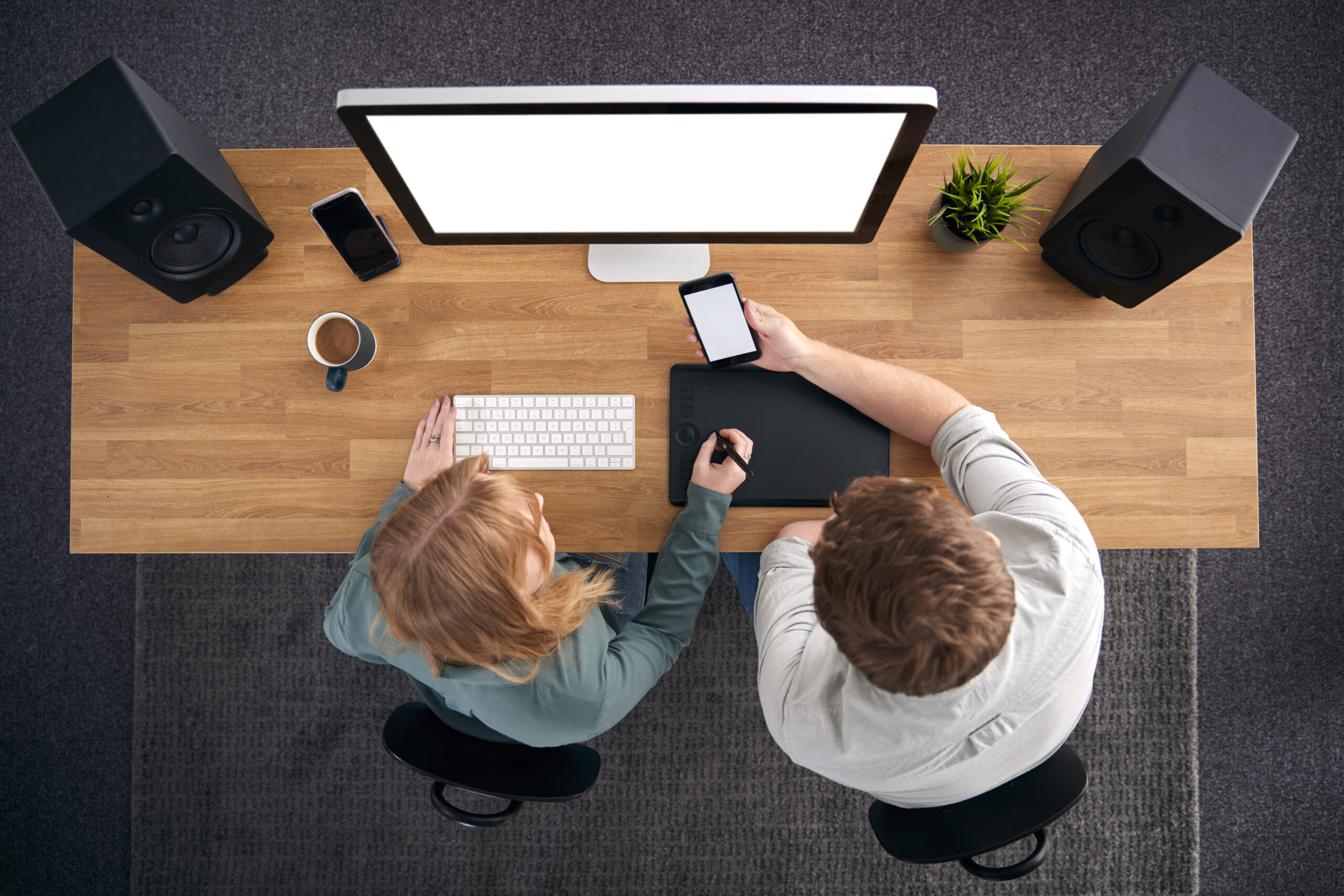Overhead View Of Male And Female Graphic Designers Working At Computer Looking At Mobile Phone